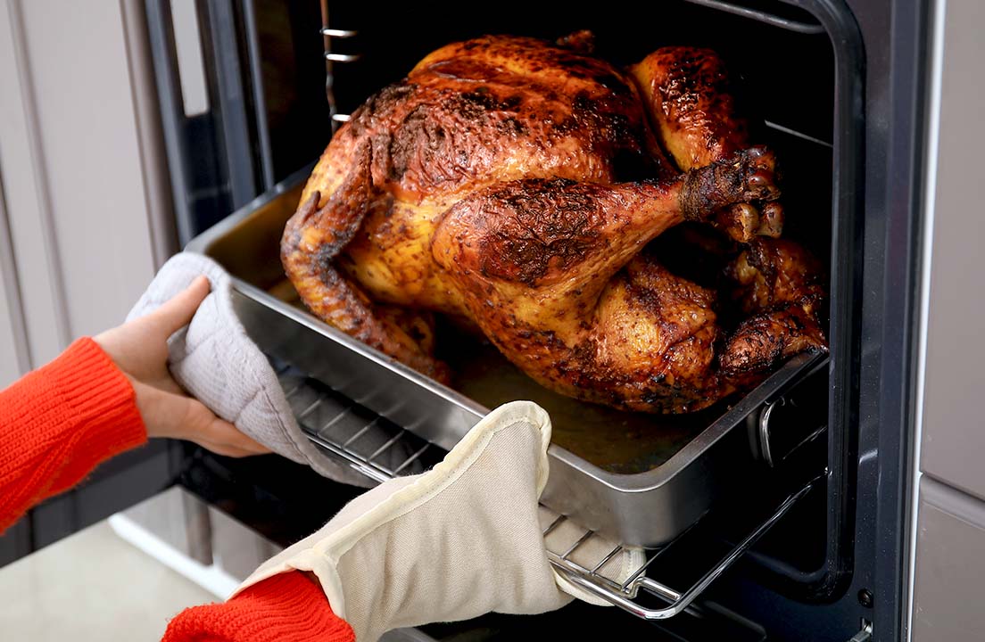Person removes a roasted turkey from the oven using oven mitts